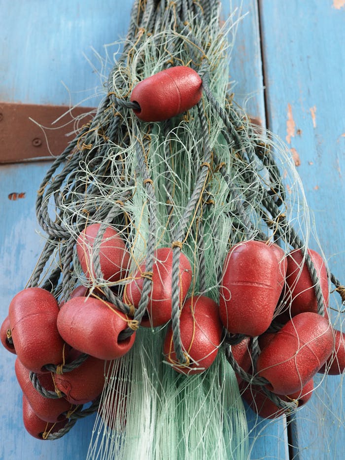 Tangled fishing nets with red floats hang on a blue wooden background, showcasing textures and vibrant colors.