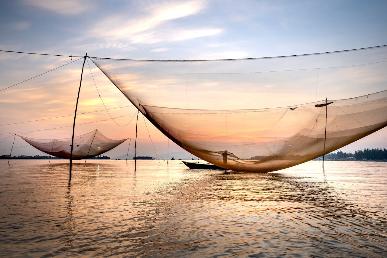 Silhouette of distant unrecognizable man floating on boat on rippling sea near fishing nets while catching fish in evening time