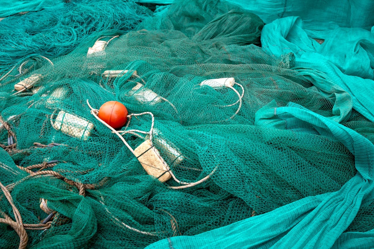 High angle of fishing net with floats and ropes against creased green fabric in daytime